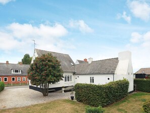 A two-story house with a gravel driveway, a tree with red flowers, and a hedge.