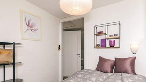 Ein Schlafzimmer mit einem Bett, einem Regal mit Büchern und Dekoration, einem gerahmten Bild und einer Pendelleuchte.