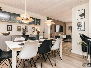 A modern dining area with a white table, black and white chairs, pendant lights, and a TV mounted on the wall. - 8 Person Holiday Home in Bagenkop (Sydlangeland)