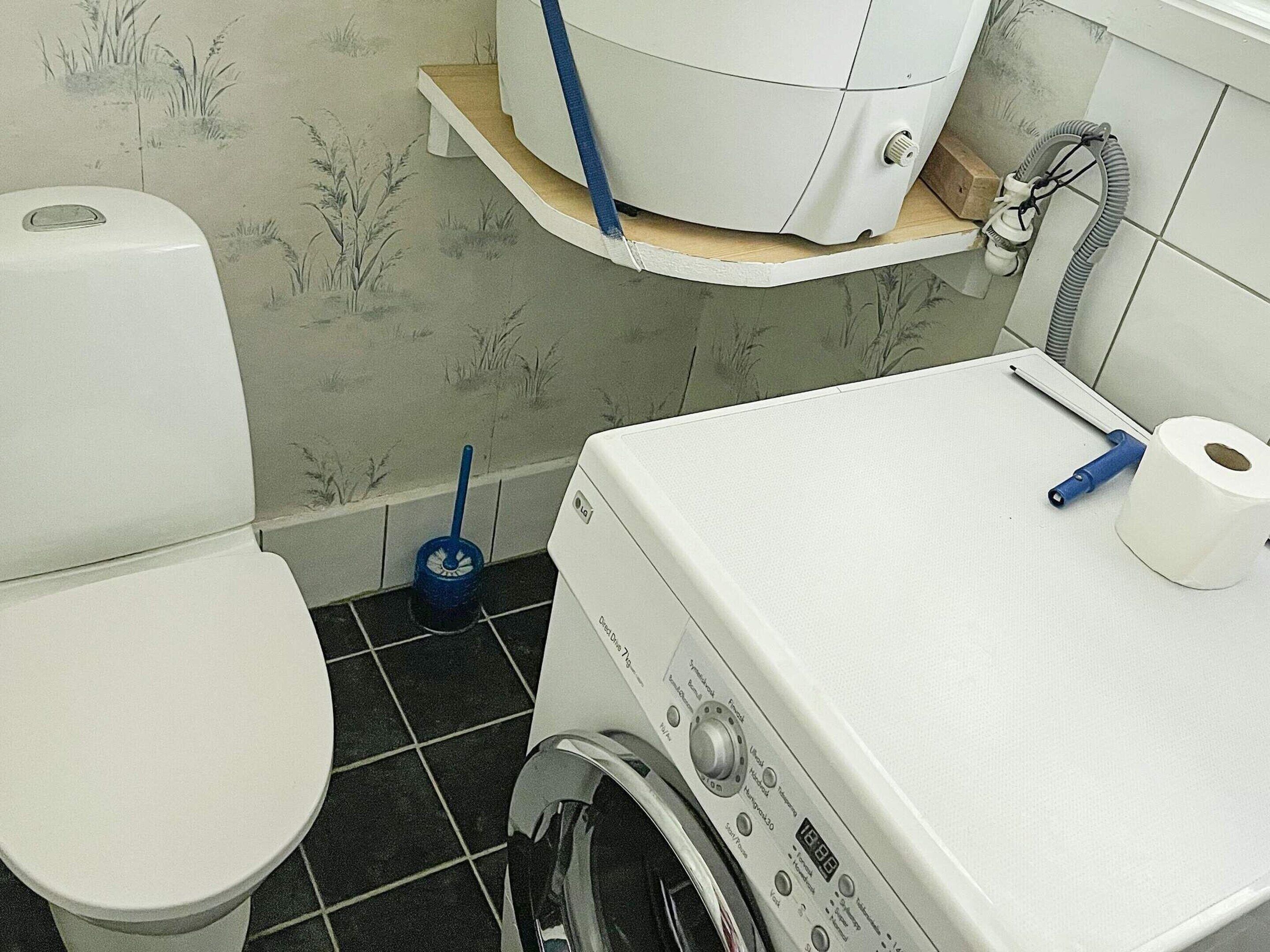 A compact bathroom with a toilet, washing machine, and a shelf above the washing machine.