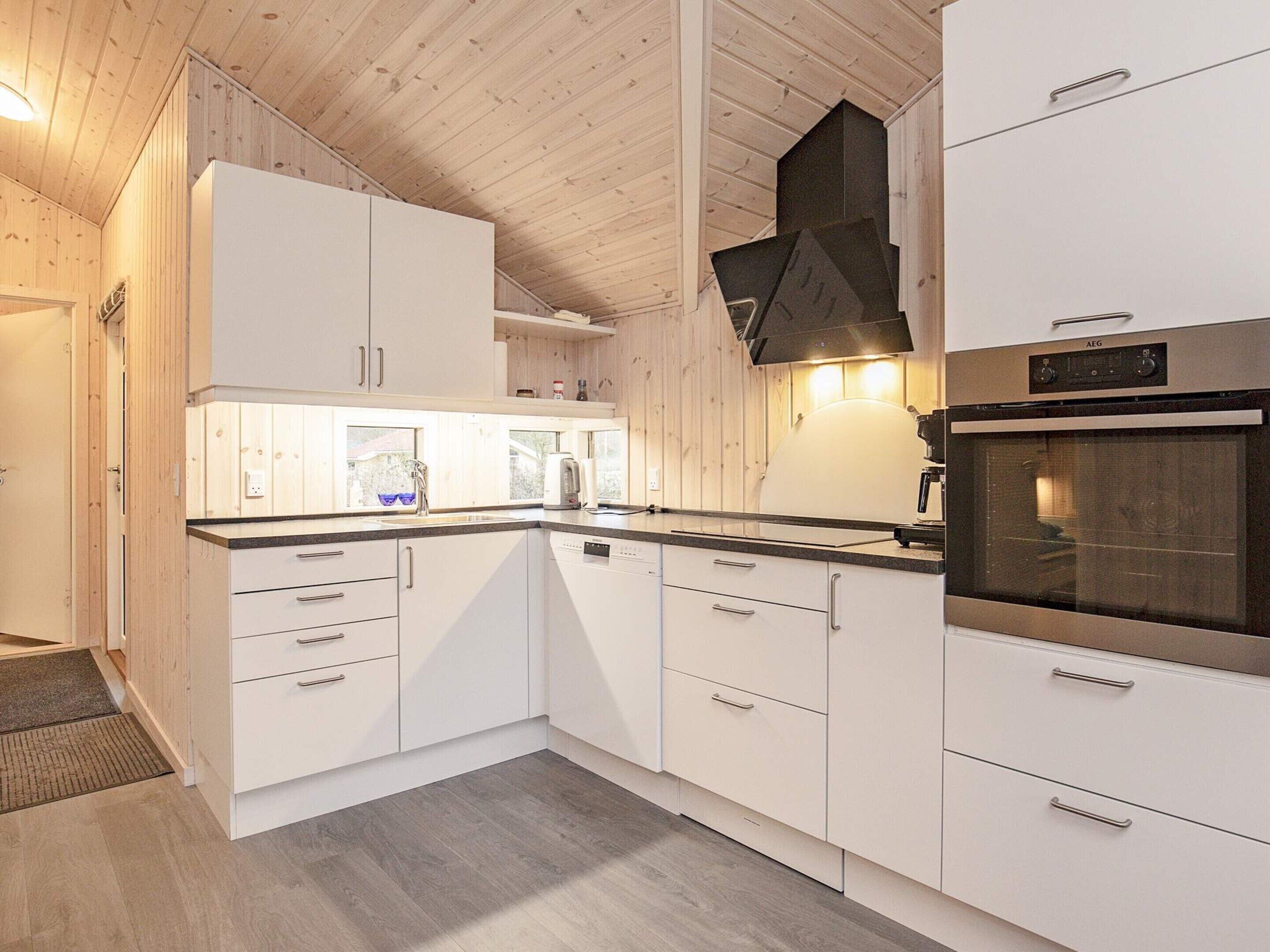 A modern kitchen with white cabinetry, a built-in oven, and a wooden ceiling.
