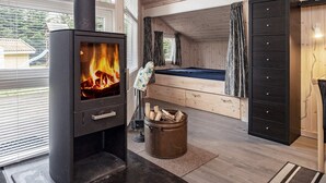 Quarto aconchegante com lareira a lenha, cama, cômoda e vista para o exterior.