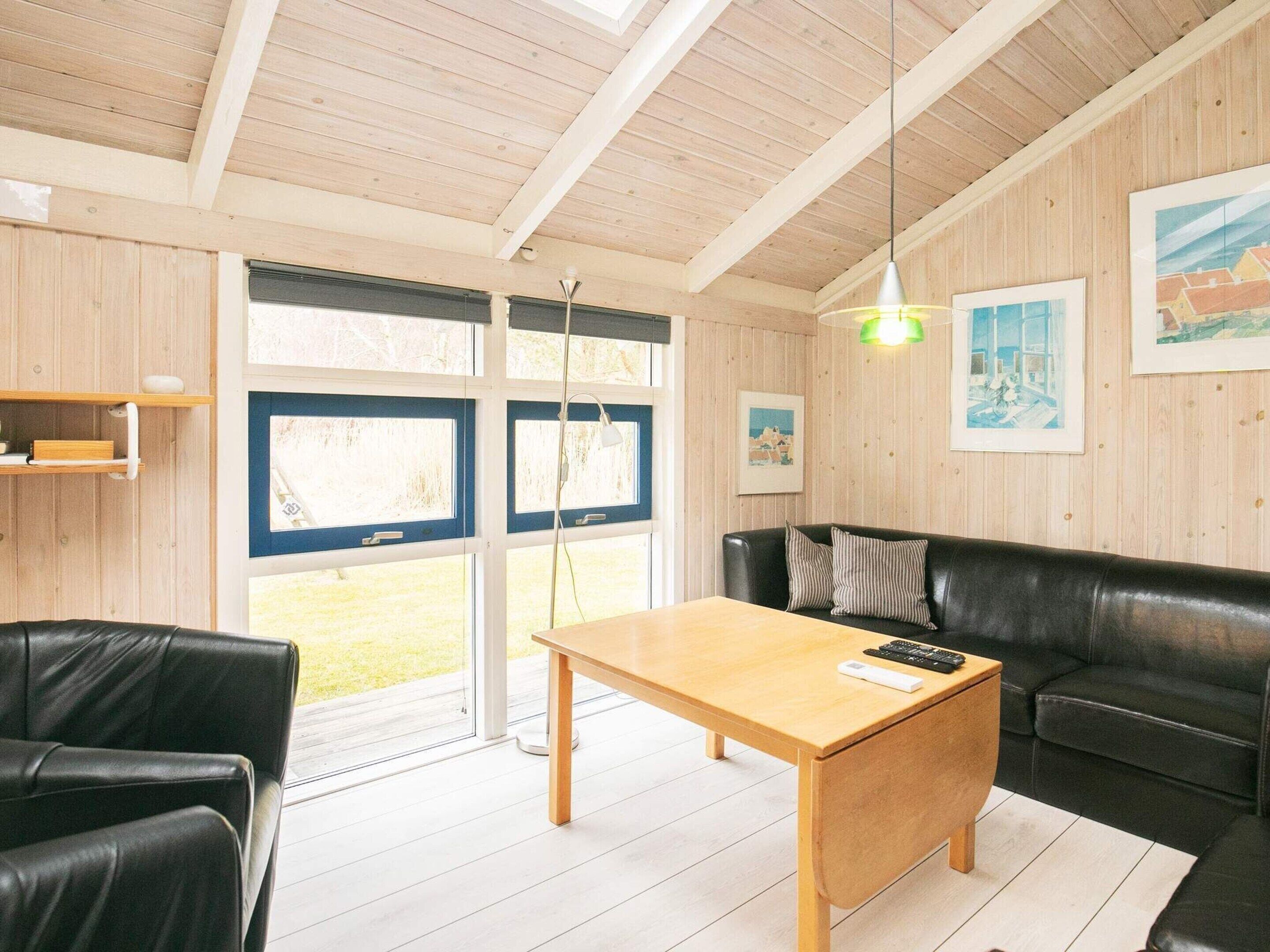 A modern living room with a wooden table, black leather sofa, and a large window with a view of the outdoors.