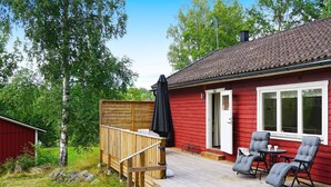 Une maison rouge avec une terrasse en bois, deux chaises, une table et un espace abrité.