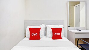 A hotel room with a bed, two red pillows with "OYO" text, a white bedside table, and a mirror. - OYO Flagship  90789 Genteng Residence (Surabaya)