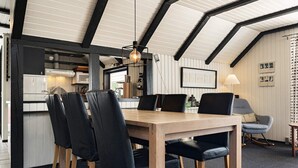 A modern dining area with a wooden table and black chairs, a kitchen in the background, and a ceiling with exposed beams. - 6 Person Holiday Home in Blavand (Blavand)