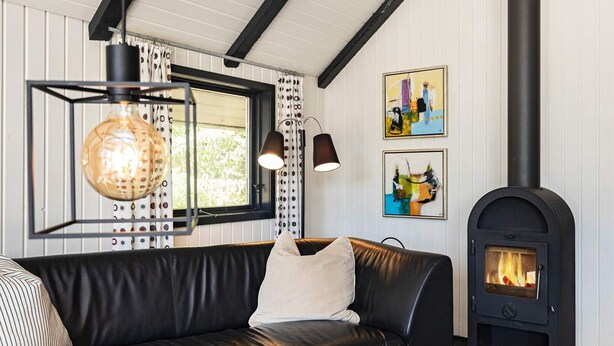 A cozy living room with a black leather sofa, a glass pendant light, a fireplace, and two framed artworks on the wall. - 6 Person Holiday Home in Blavand (Blavand)