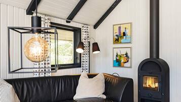 Una sala de estar acogedora con un sofá de cuero negro, una lámpara colgante de cristal, una chimenea y dos obras de arte enmarcadas en la pared.