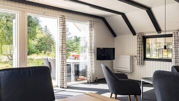 Una habitación acogedora con una mesa de madera, dos sillas, un televisor y un ventanal con cortinas.