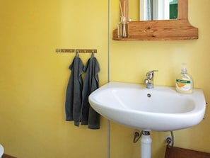 A bathroom with a white sink, a wooden shelf with a mirror, and two towels hanging on a metal rack.