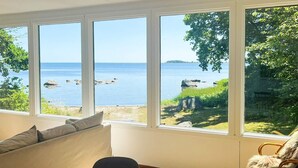 A room with a large window overlooking a body of water, a wooden table, a sofa, and a rocking chair. - 4 Star Holiday Home in Solvesborg (Sölvesborg)