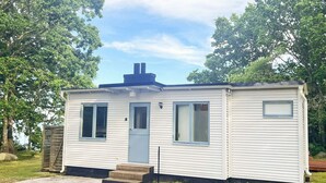A single-story mobile home with a front door, two windows, a chimney, and a small porch. - 4 Star Holiday Home in Solvesborg (Sölvesborg)