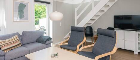 A modern living room with a sofa, two chairs, a table, a TV, and a staircase.