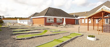 A building with a brick exterior, a covered patio area, and a gravel ground with green artificial grass.