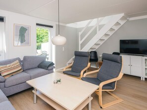 A modern living room with a sofa, two chairs, a table, a TV, and a staircase.
