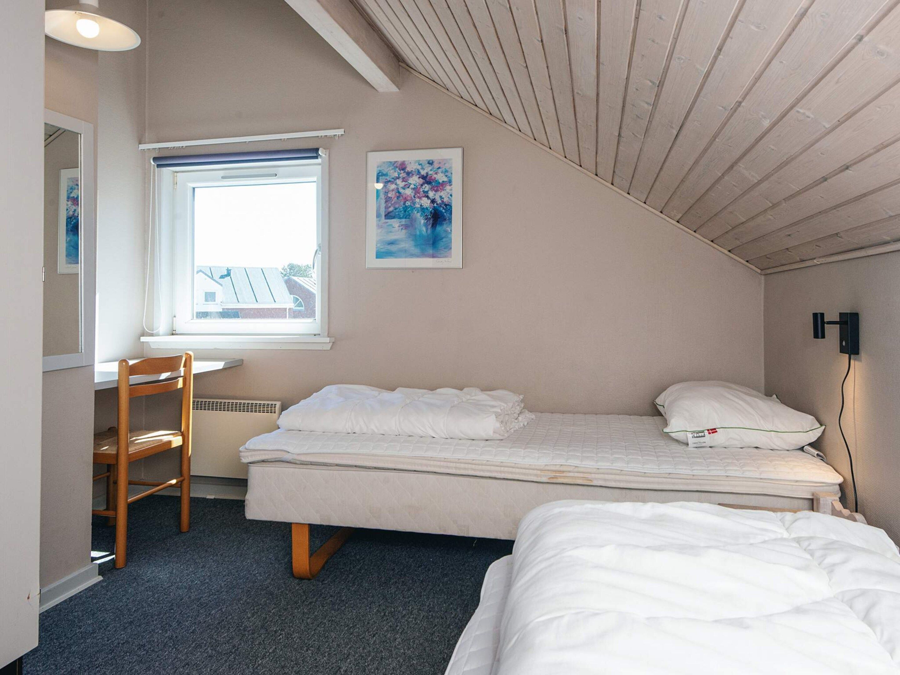A small, well-lit room with a single bed, a desk, and a window.