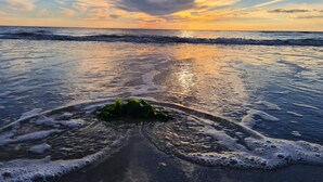 Een strand met golven, een heldere lucht en een zonsondergang.