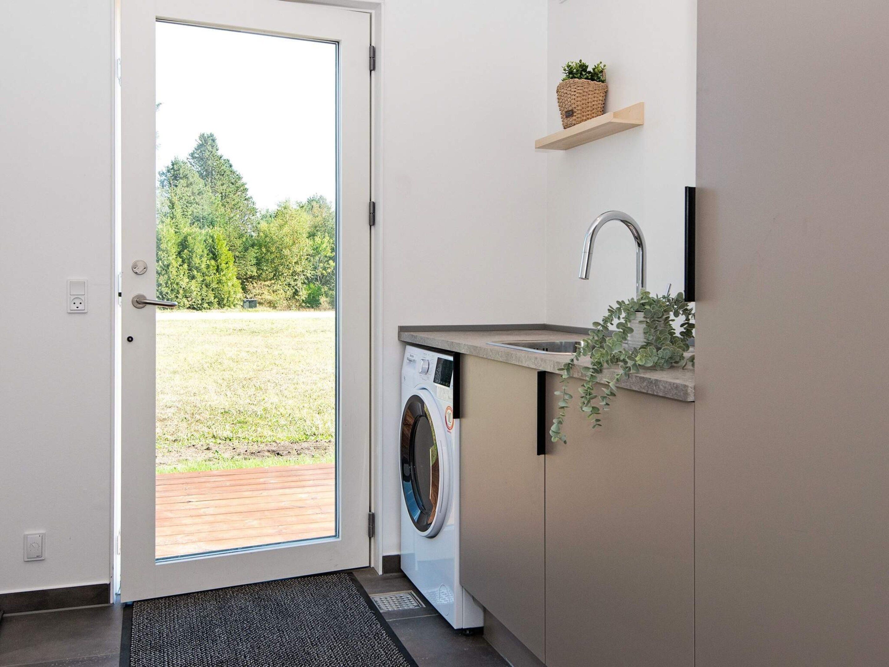 Een wasserette met een wasmachine, een wasbak en een deur naar een buitenruimte.