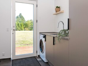 Une buanderie équipée d’un lave-linge, d’un évier et d’une porte donnant sur un espace extérieur.