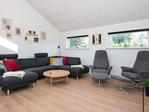 Un salon moderne avec un canapé gris, deux fauteuils, une table basse ronde et des œuvres d’art accrochées aux murs.