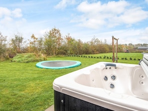 En baghave med jacuzzi, trampolin og græsplæne.