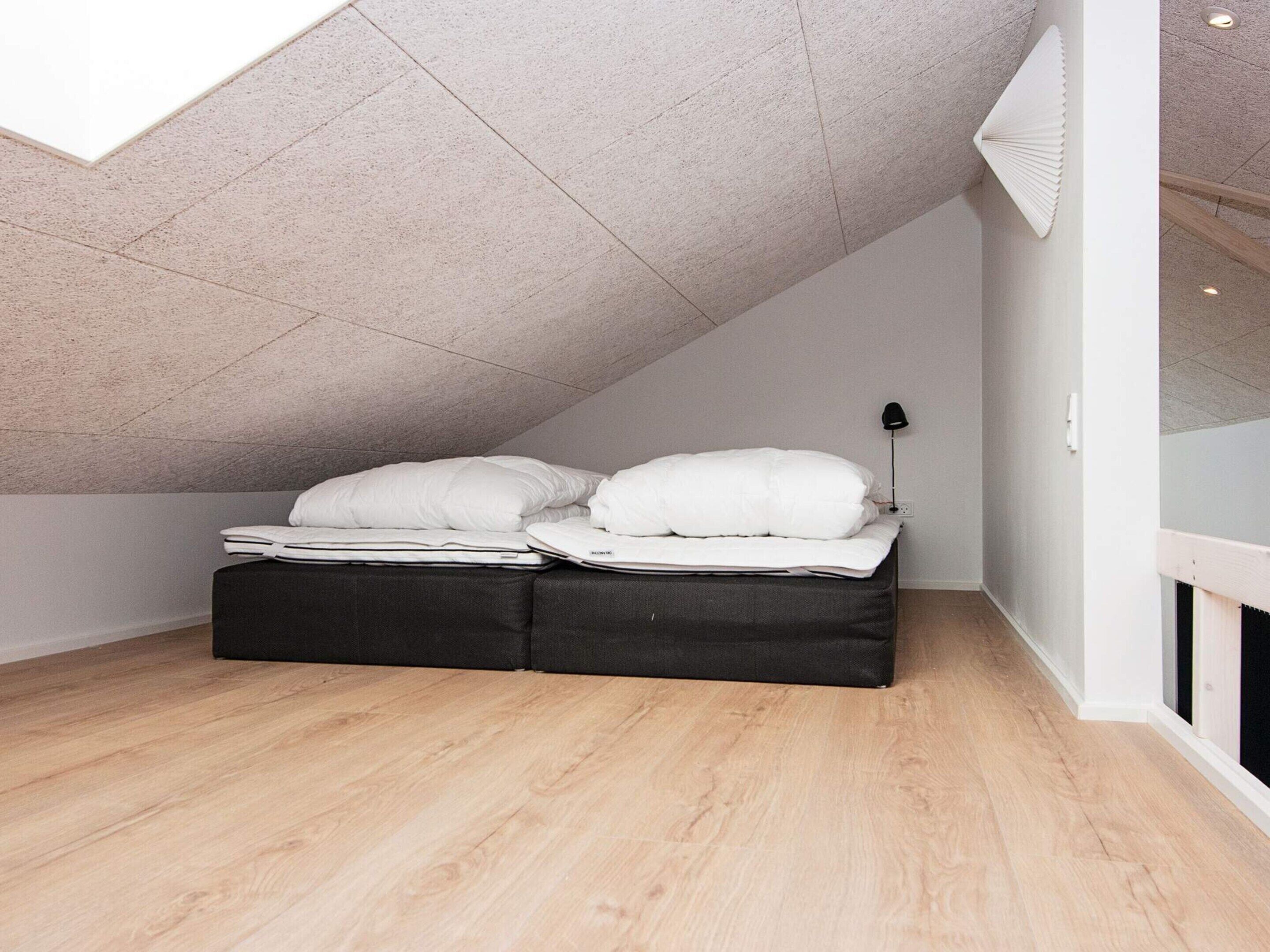 A bedroom with a sloped ceiling, a bed with white bedding, a black headboard, and a bedside lamp.