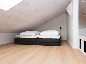 Une chambre à coucher avec un plafond en pente, un lit avec une literie blanche, une tête de lit noire et une lampe de chevet.