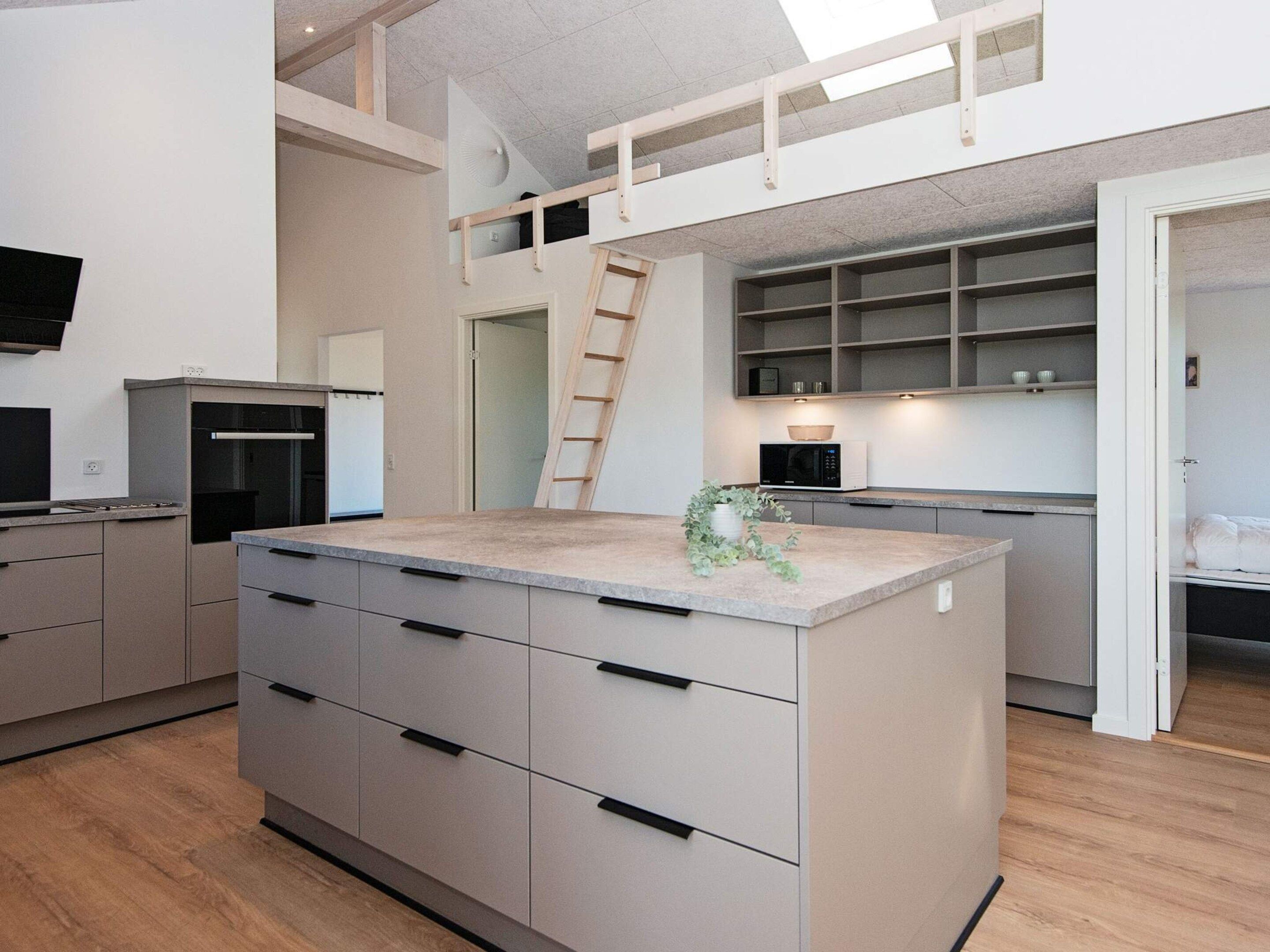 Cocina moderna con una isla central, electrodomésticos integrados y un entrepiso con habitación.