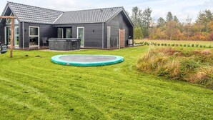 Una casa moderna con un amplio patio trasero, que incluye un trampolín, un jacuzzi y una zona de estar al aire libre.