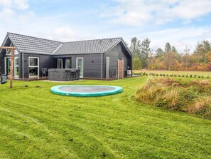 A modern house with a large backyard, including a trampoline, a hot tub, and a patio area.