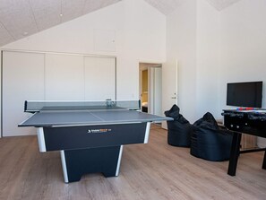 A ping pong table, a foosball table, and a television in a room with wooden flooring and white walls.