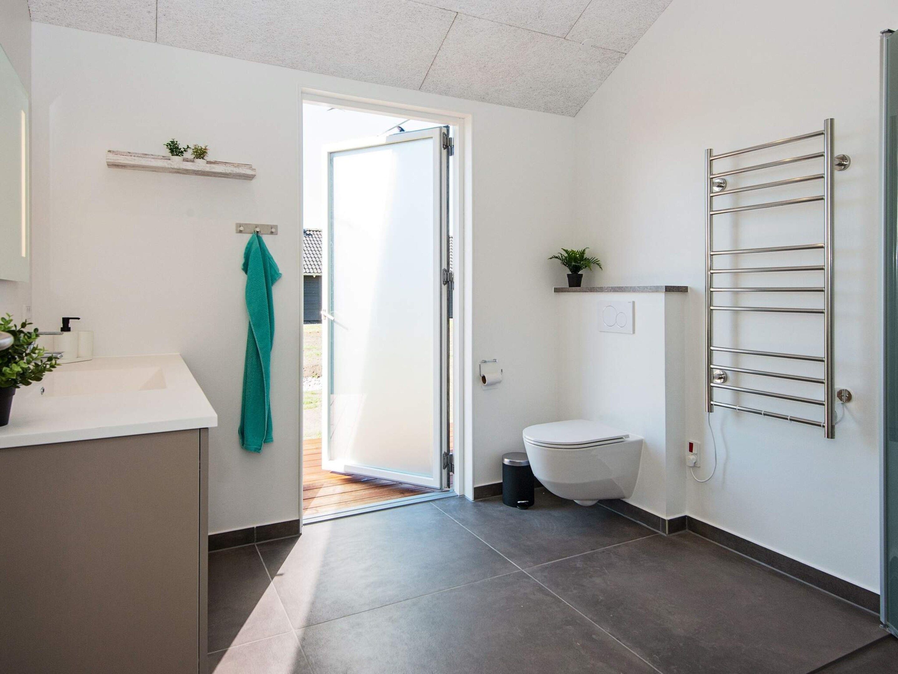 A modern bathroom with a white sink, a toilet, a towel rack, and a shower area.