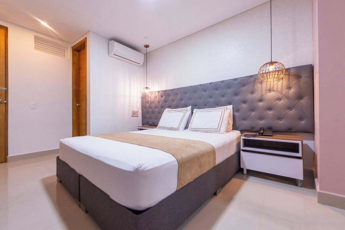 A modern bedroom with a tufted headboard, a bedside table with a lamp, and a built-in wardrobe.