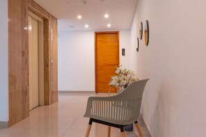 A modern interior with a wooden door, a grey chair, and a vase with white flowers. - Infinity Hotel (Medellín)