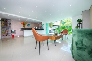 A hotel lobby with a reception desk, a seating area with two chairs, a green sofa, and a plant. - Infinity Hotel (Medellín)