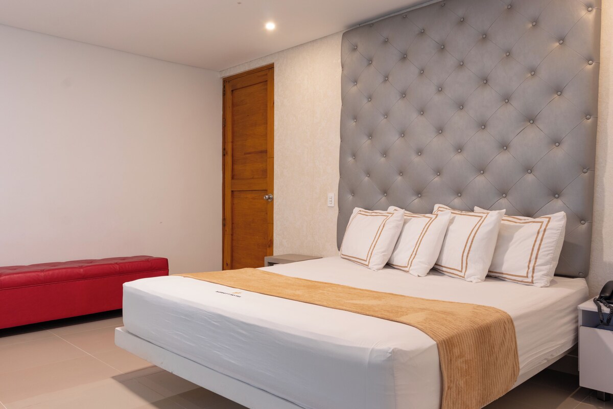 A modern bedroom with a large bed, a red bench, and a wooden door.