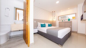 A modern hotel room with a large bed, a bathroom with a sink and toilet, and a mirror above the bed.