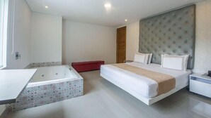 A modern bedroom with a large bed, a separate bathtub, and a red bench.