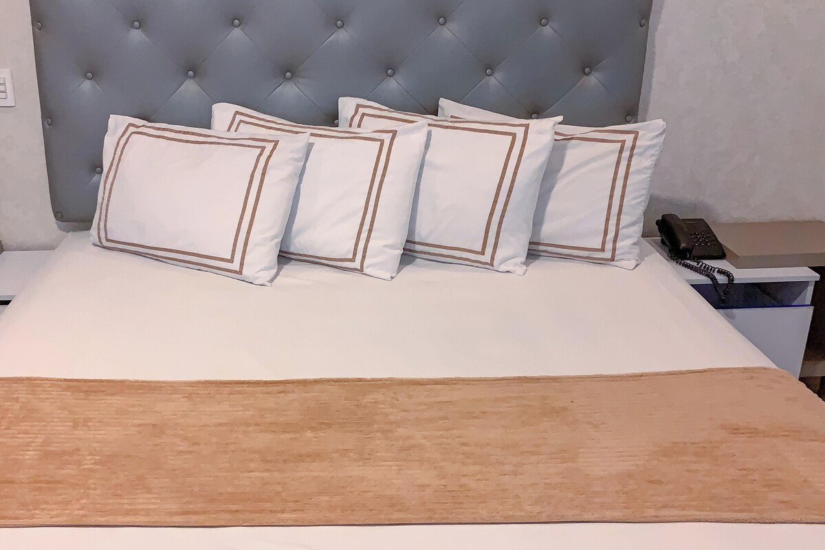 A neatly made bed with a brown throw blanket, a tufted headboard, and white pillows with brown trim.