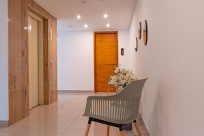 A hallway with a wooden door, a grey chair, and a vase of flowers. - Infinity Hotel (Medellín)