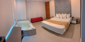 Een moderne hotelkamer met een groot bed, een rode poef, een badkuip en een nachtkastje met een telefoon.
