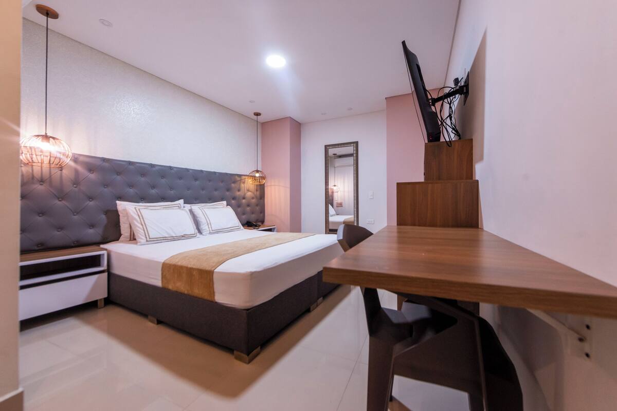 A modern hotel room with a large bed, bedside tables, a wooden desk, and a television mounted on the wall.