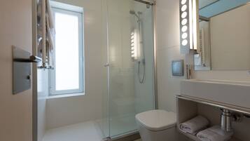 Un baño moderno con ducha de vidrio, inodoro y tocador con espejo e iluminación.