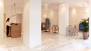 Un moderno vestíbulo de hotel con mostrador de recepción, zona de estar y una gran planta en maceta.
