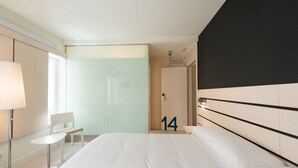 Habitación de hotel con una cama grande, un escritorio, una silla y un vidrio que da al baño.