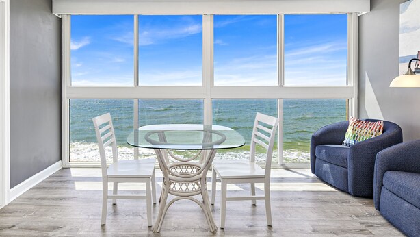 Une pièce moderne avec une table et des chaises en verre, un canapé bleu et une grande fenêtre donnant sur l’océan.
