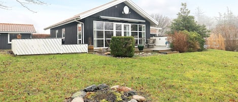 Ett hus med en stor trädgård framför, en eldstad och ett förråd.