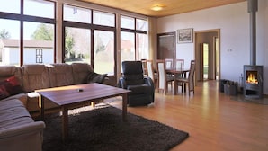A spacious living room with a large window, a fireplace, a sofa, a dining table, and a chair. - 6 Person Holiday Home in Kirke Hyllinge (Kirke Hyllinge)