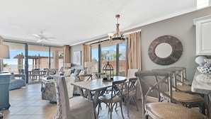 Un vaste espace de vie comprenant un coin repas avec une table, des chaises et un lustre. Une grande fenêtre offre une vue sur l’extérieur.