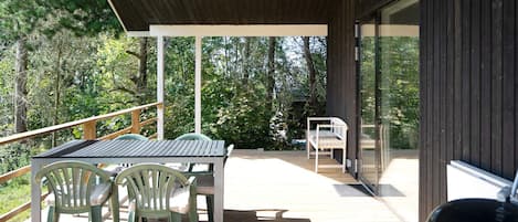 An outdoor deck with a table and chairs, a barbecue grill, and a view of the surrounding forest.